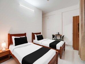 A hotel room with two wooden beds, a bedside table with a lamp, a small table with chairs, and a wooden wardrobe. - Hotel O K R Puram Manyata (Bengaluru)