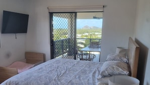 Ein Schlafzimmer mit Bett, Fernseher, Balkon mit Tisch und Stühlen und Blick ins Freie.