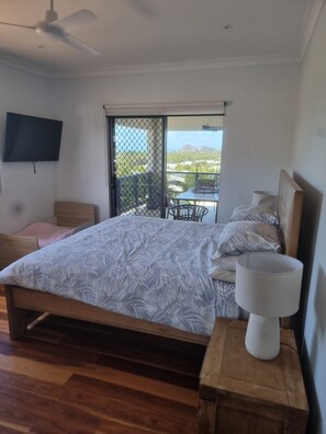Un dormitorio con cama, televisor, balcón con mesa y sillas, y vistas al exterior.
