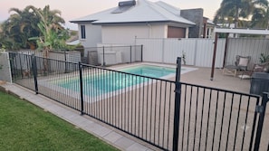 Un patio trasero con piscina, área cercada y mobiliario exterior.