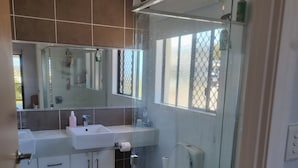 Ein modernes Badezimmer mit Duschkabine aus Glas, einer weißen Toilette und einem Waschbecken mit Spiegel darüber.