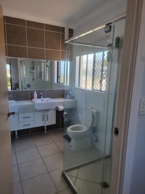 Un baño moderno con cabina de ducha de vidrio, inodoro blanco y lavamanos con espejo.