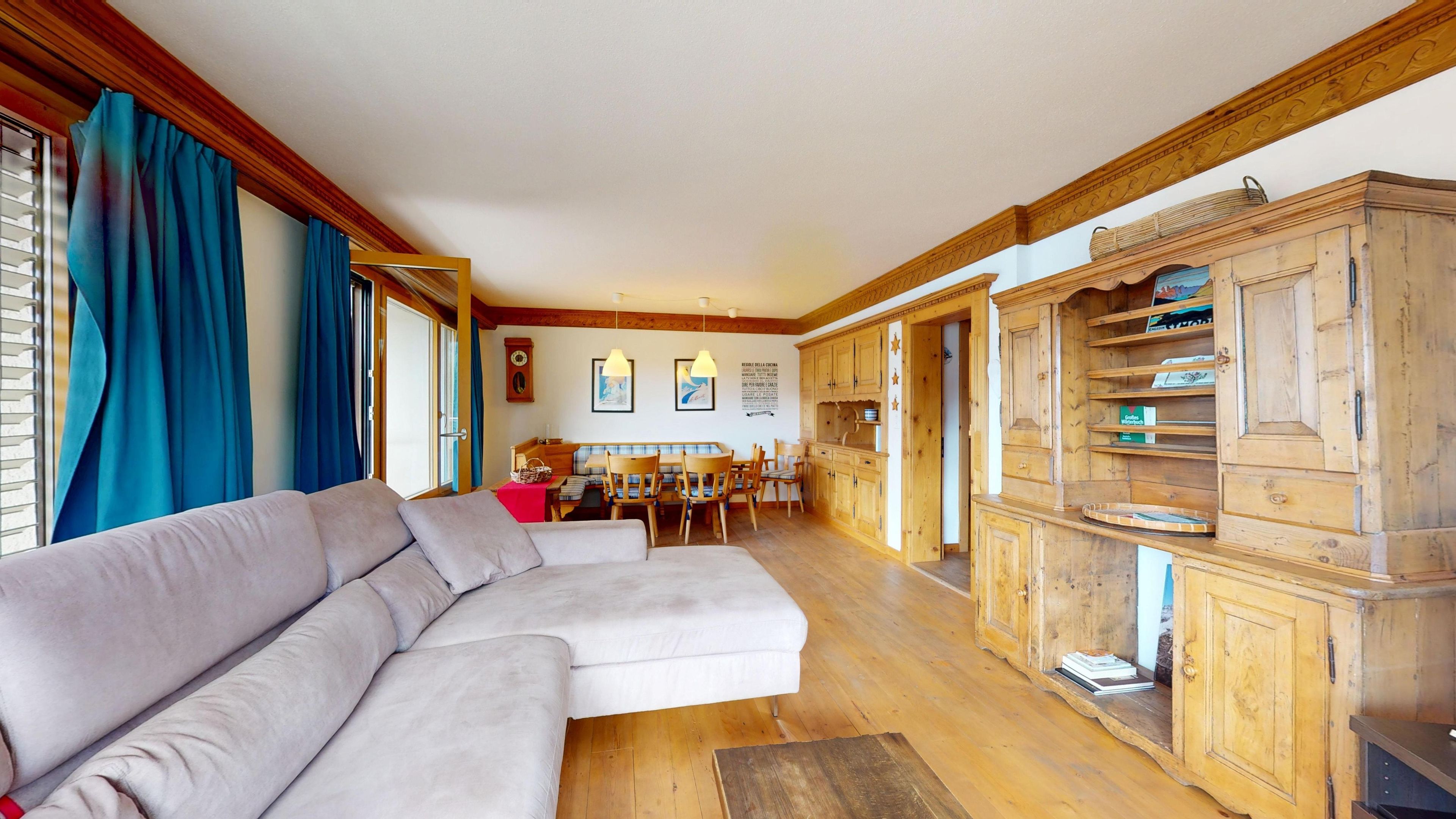 Ein Wohnzimmer mit einem Ecksofa, Holzschränken und einem Essbereich mit einer Bank.