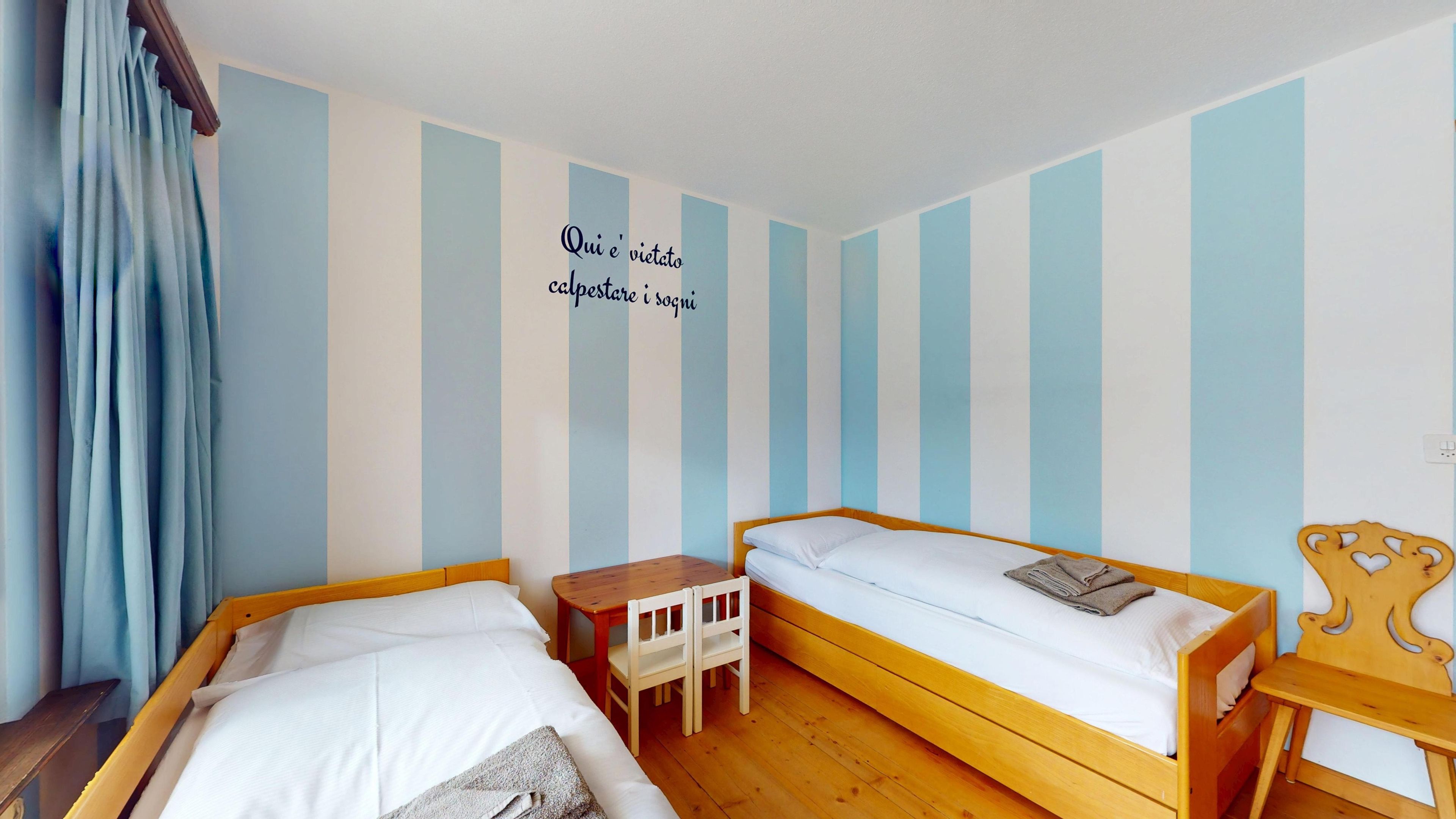 Ein Zimmer mit zwei Holzbetten, einem kleinen Tisch und einer Wand mit vertikalen Streifen.