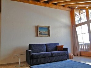 A room with a sofa, a painting, and a window. - Two-room apartment on the top floor (4th floor), approximately 60 m². (Celerina/Schlarigna)