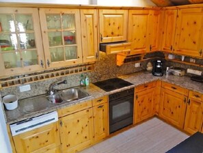 A kitchen with wooden cabinets, a sink, a dishwasher, and a coffee maker. - Two-room apartment on the top floor (4th floor), approximately 60 m². (Celerina/Schlarigna)