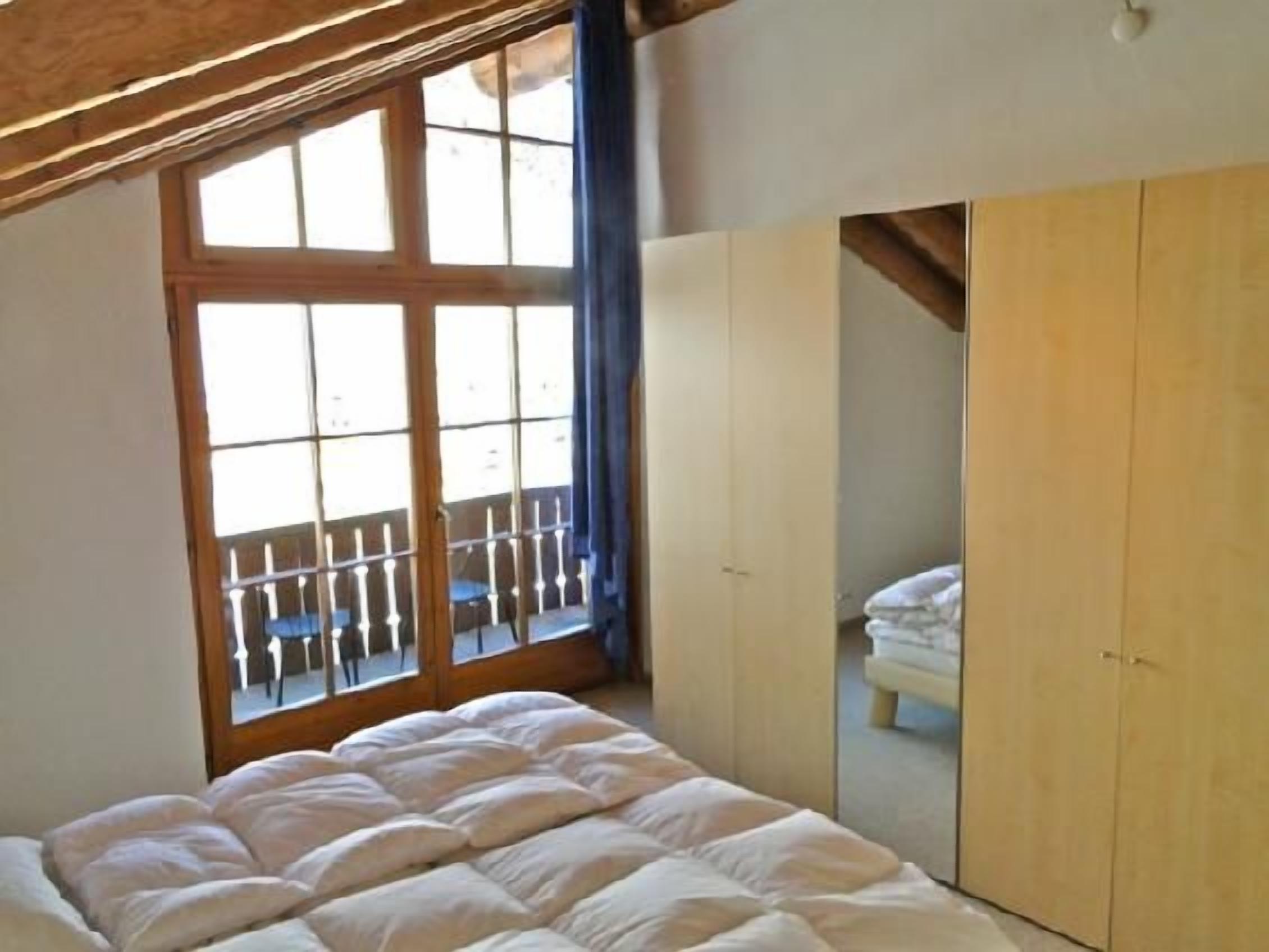 Ein Schlafzimmer mit einem Bett, einem Kleiderschrank und einem Fenster mit Blick auf einen Balkon.
