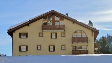 Ein zweistöckiges Gebäude mit einem Balkon im oberen Geschoss, großen Fenstern und einem mit Schnee bedeckten Grund.