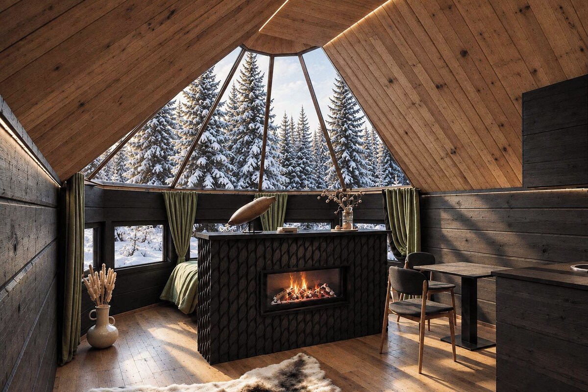 A cozy cabin interior with a wooden ceiling, a fireplace, a dining area, and a view of snow-covered trees.