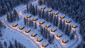 A snow-covered landscape with multiple cabins arranged in a circular pattern, connected by winding paths.