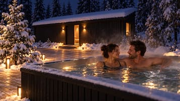 A couple in a hot tub with a wooden deck and a cabin in the background.