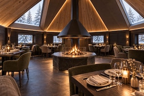 Un restaurante con una chimenea central, paredes de madera y varias mesas de comedor.