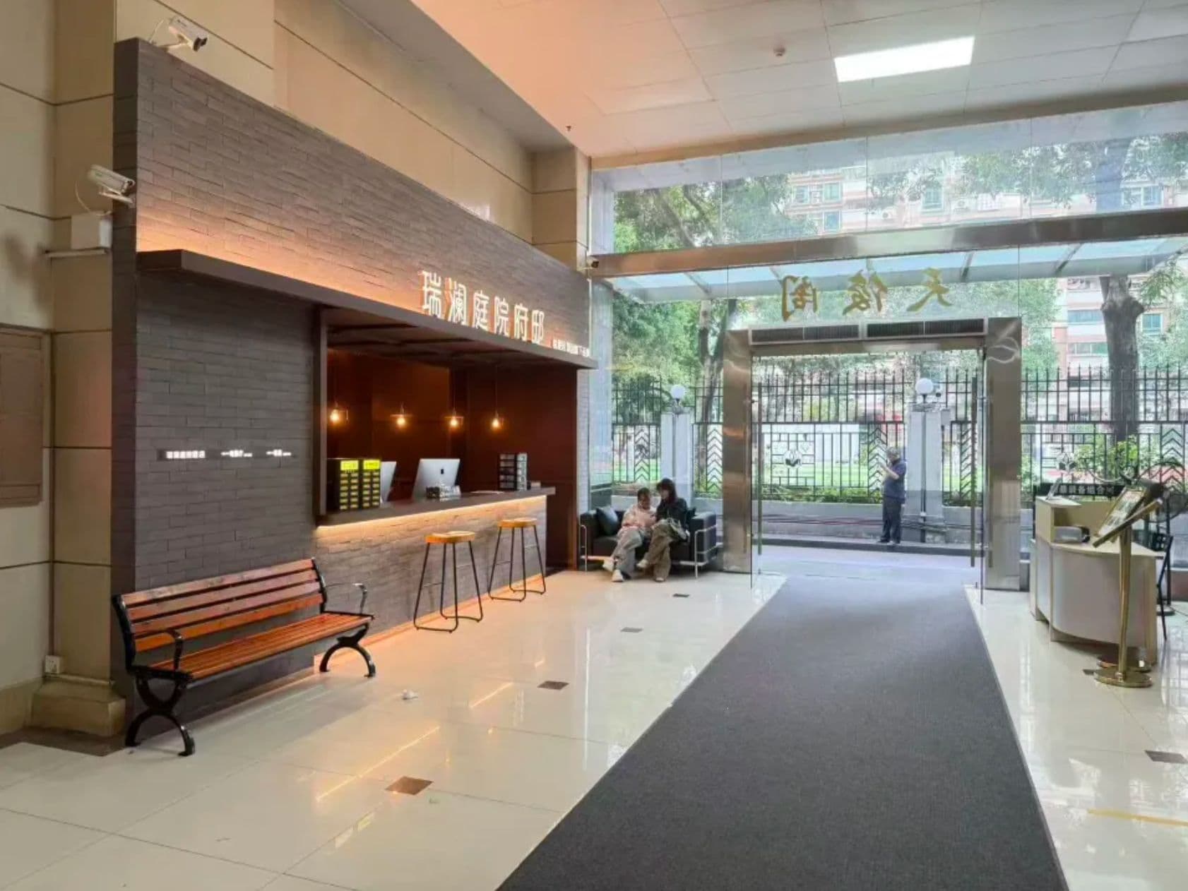 Una zona de recepción con un banco, un mostrador con una computadora y una entrada con reja.