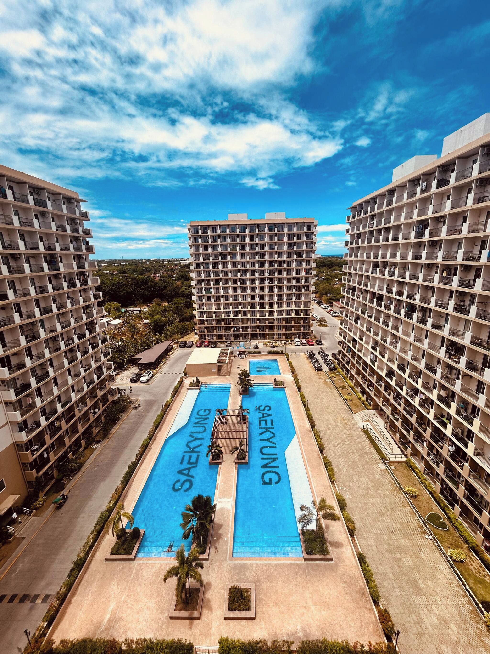Un immeuble de grande hauteur doté de nombreux balcons et d’un espace piscine central arborant la marque « SAEKYUNG ».
