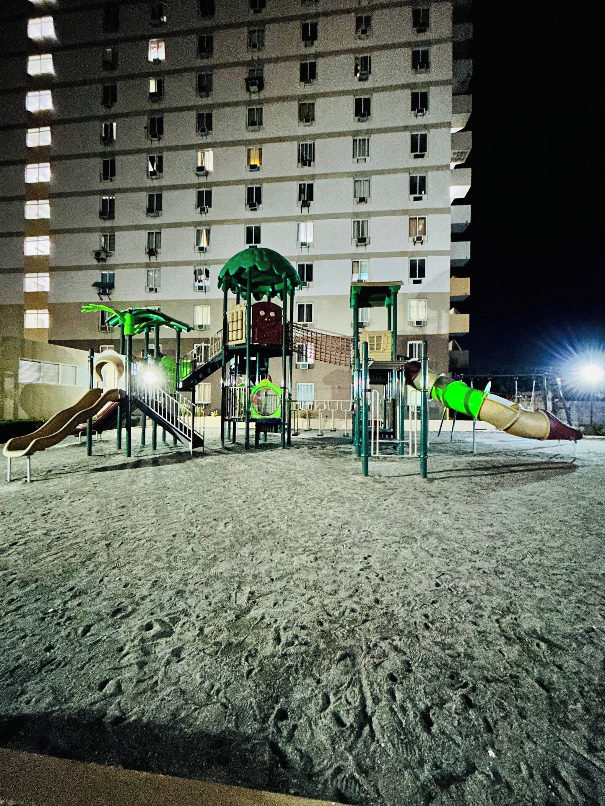 A playground with slides and climbing structures, located in front of a multi-story building with windows.