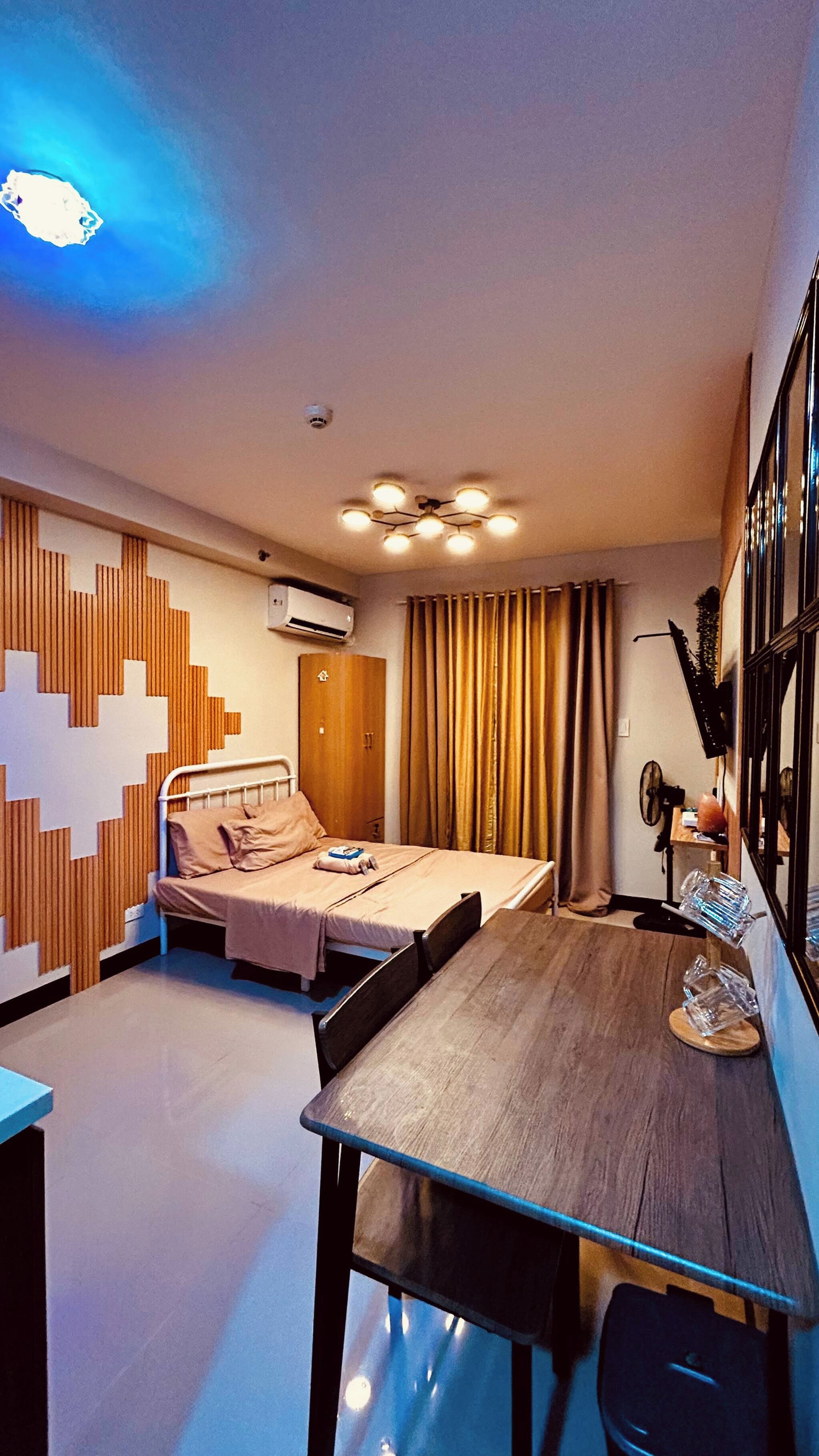 A hotel room with a bed, a desk, a chair, a wardrobe, a mirror, and a ceiling light fixture.