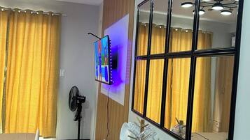 A dining area with a wooden table, chairs, a wall-mounted TV, and a large mirror reflecting the room.