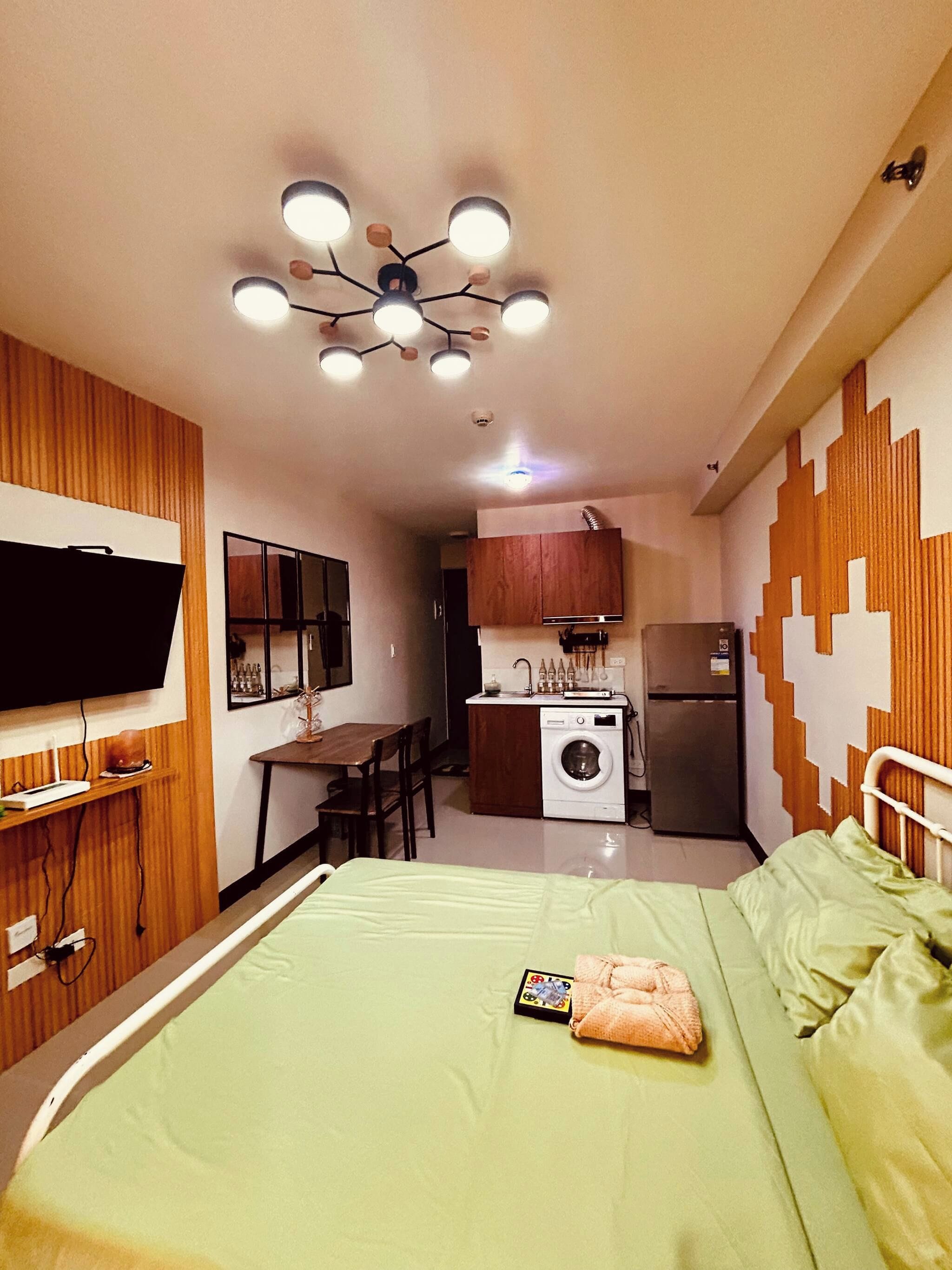 Habitació d'hotel senzilla amb llit, petita cuineta, televisió i llum penjant del sostre.