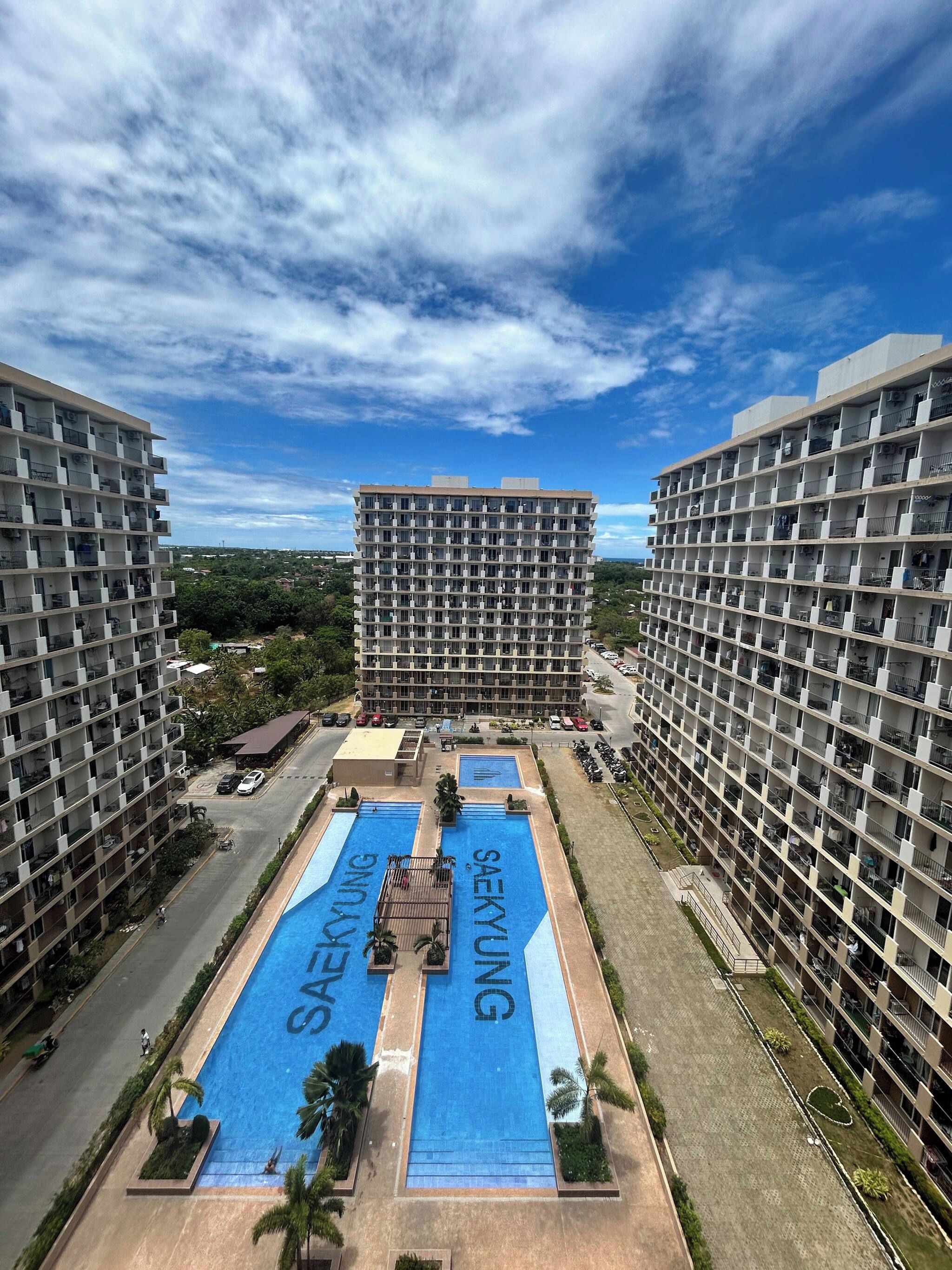 Un edificio de gran altura con varios balcones, una piscina central y una zona de estacionamiento.