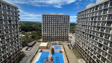 Un edificio de gran altura con varios balcones, una piscina central y una zona de estacionamiento.