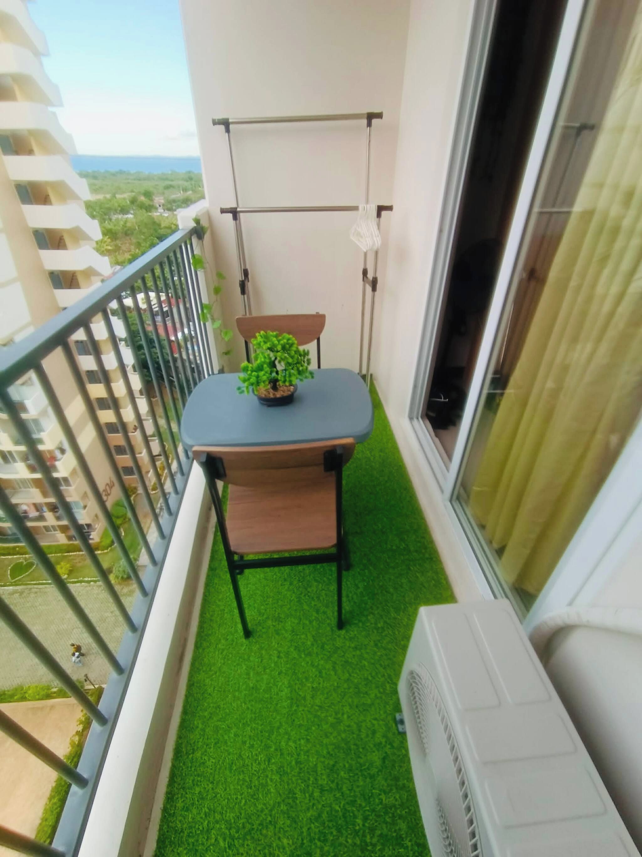 Un balcón con una pequeña mesa, una silla, una planta en maceta y una ventana con cortinas.