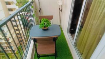 Un balcón con una pequeña mesa, una silla, una planta en maceta y una ventana con cortinas.