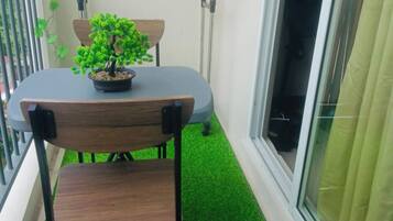A balcony with a table and chairs, a potted plant, a hanging light fixture, and a view through a window.