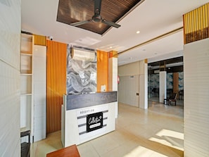 A reception area with a modern design, including a reception desk labeled 'RECEPTION Collection Company Services,' a ceiling fan, and a fire extinguisher.