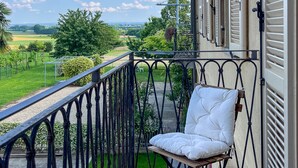 Un balcone con ringhiera in metallo, una sedia imbottita bianca e vista su un paesaggio verde.