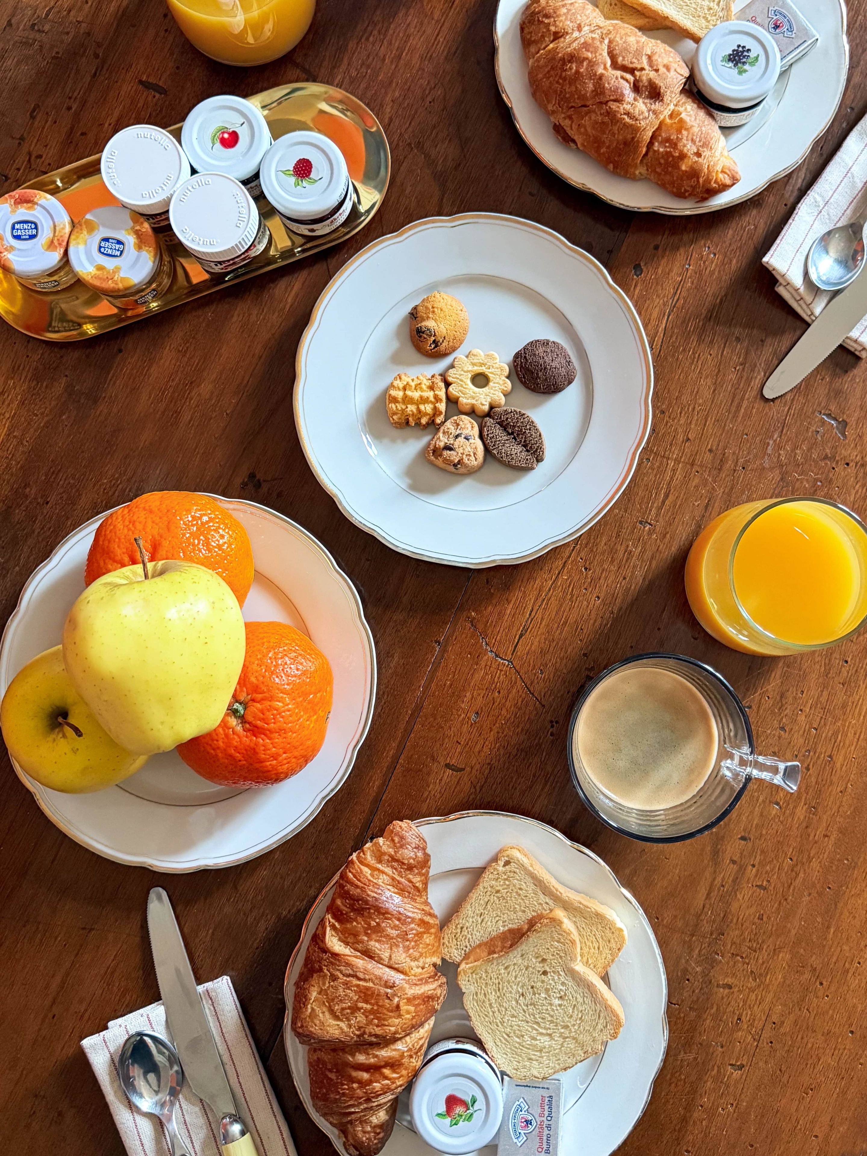 A breakfast setting with croissants, bread, fruit, and a variety of spreads on plates.
