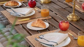 Ett picknickbord i trä, dukat med tallrikar, croissanter, äpplen och glas med apelsinjuice.