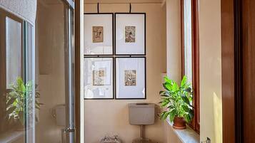 Ein schmales Badezimmer mit Toilette, Bidet und Waschbecken, einer Hängeleuchte und gerahmten Bildern an der Wand.