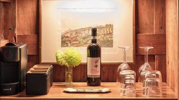 A wooden bar area with a framed picture, a bottle of wine, glasses, and a coffee machine.