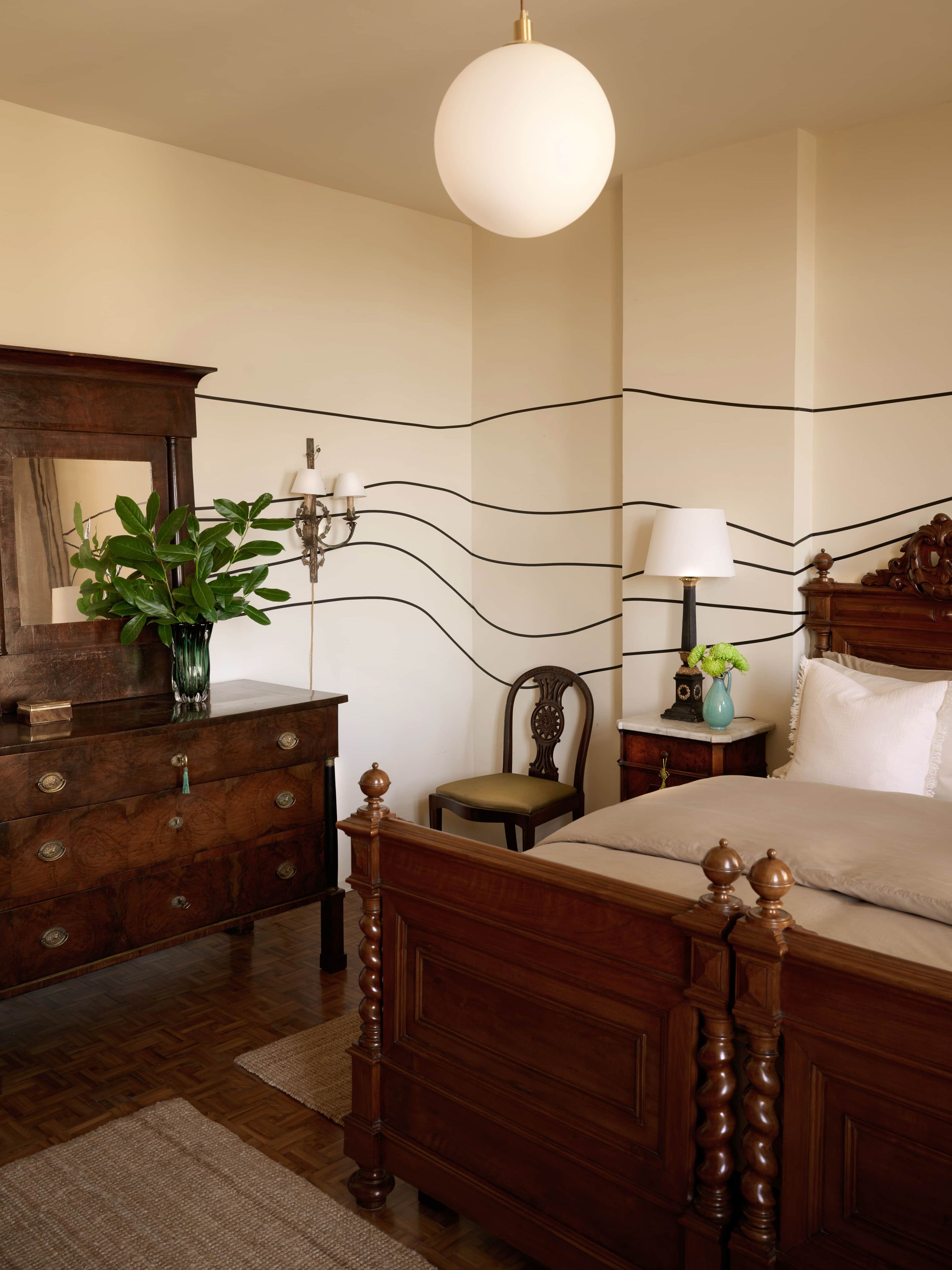 A bedroom with a wooden bed, a dresser, a mirror, a lamp, and a plant.