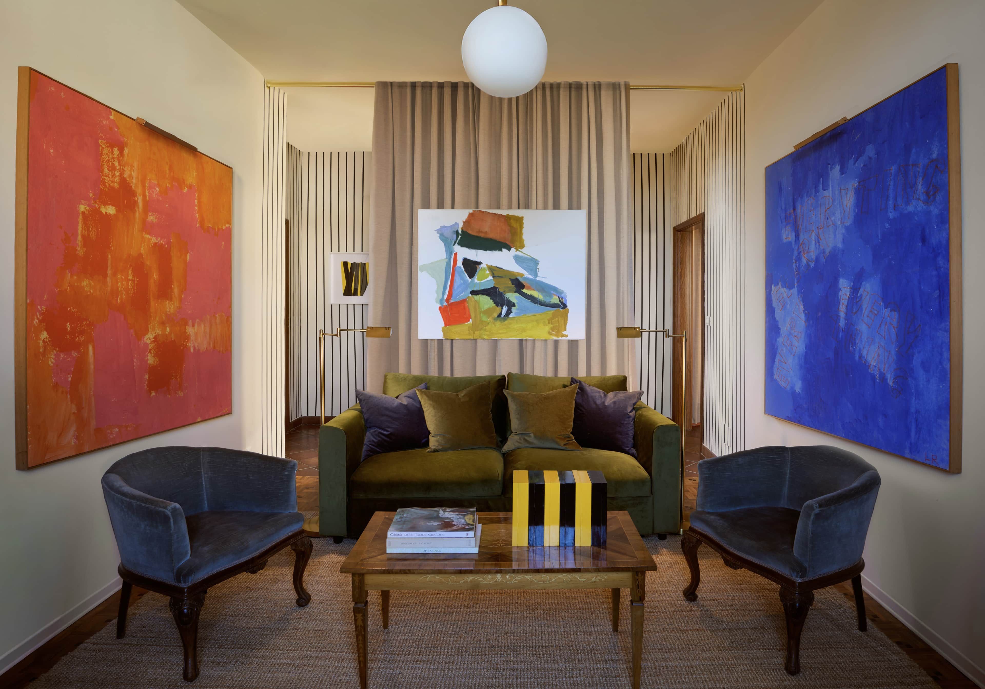 A living room with a green sofa, two armchairs, a coffee table, and three paintings.