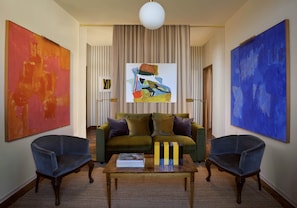 A living room with a green sofa, two armchairs, a coffee table, and three paintings.