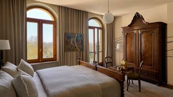 A hotel room with a large bed, a desk with a chair, a wardrobe, and two windows with curtains.