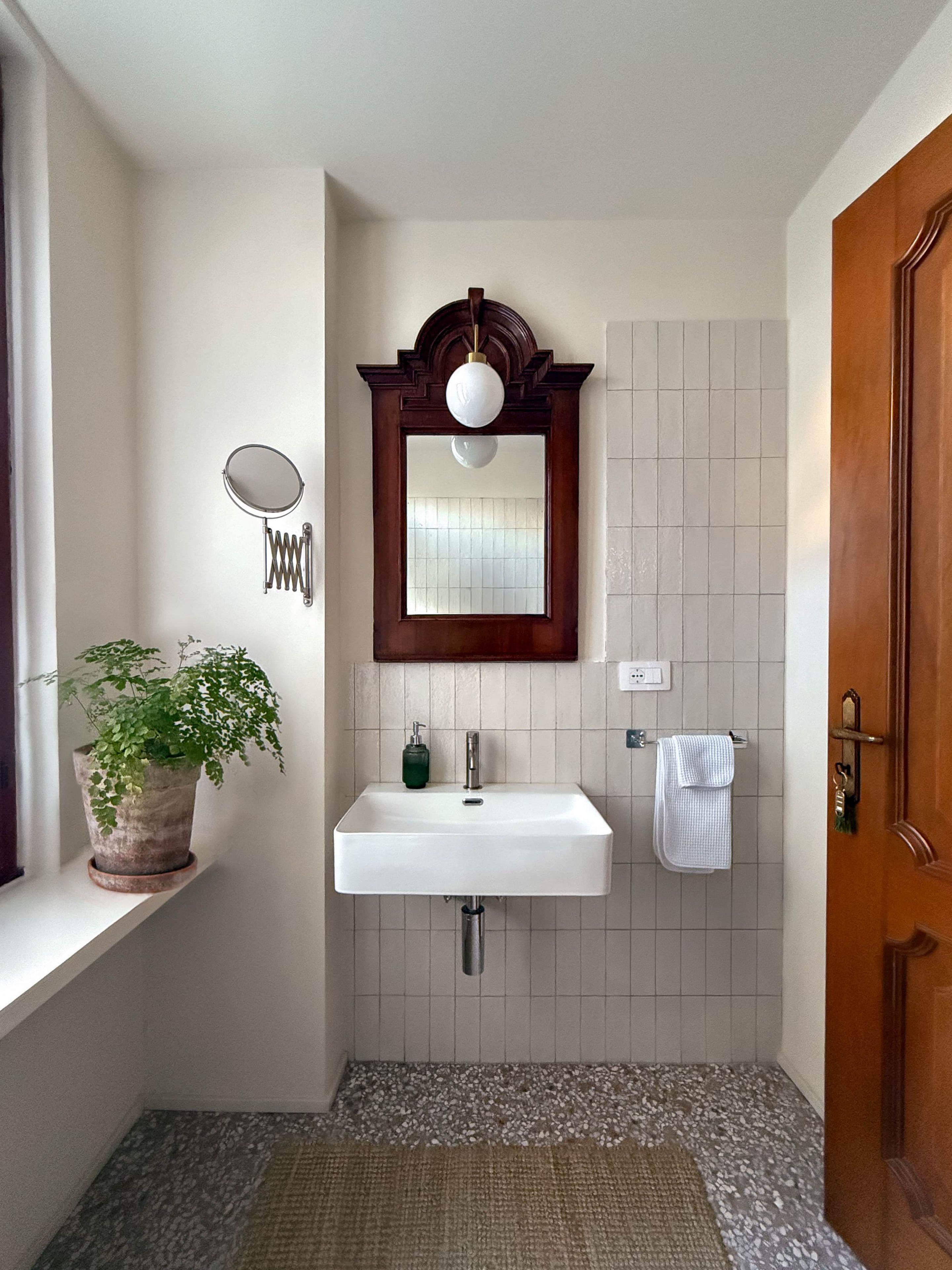 A bathroom with a white sink, a mirror, a potted plant, and a towel rack.