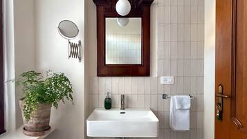 A bathroom with a white sink, a mirror, a potted plant, and a towel rack.