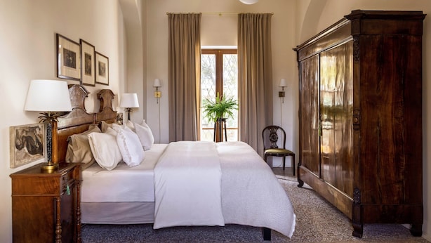 A hotel room with a large bed, two bedside tables with lamps, a wardrobe, and a window with curtains. - La Giovanna guest room features a sumptuous antique bed that (Chieri)