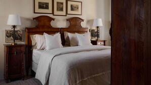 A bedroom with a large bed, two bedside tables with lamps, a wooden wardrobe, and three framed pictures on the wall. - La Giovanna guest room features a sumptuous antique bed that (Chieri)