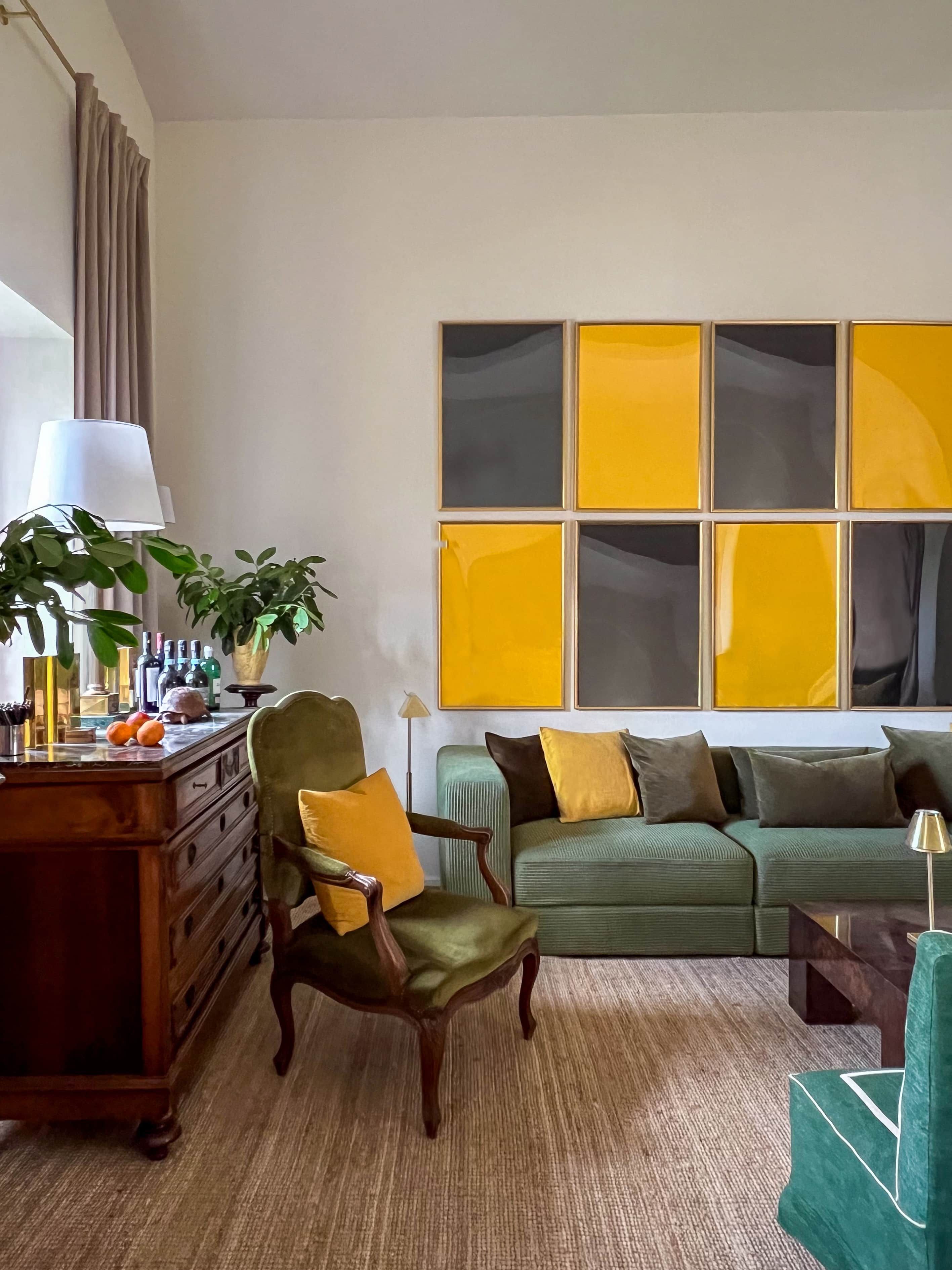 Ein Wohnzimmer mit einem grünen Sofa, einem Holzstuhl, einem Holztisch mit Lampe und einem großen abstrakten Gemälde an der Wand.