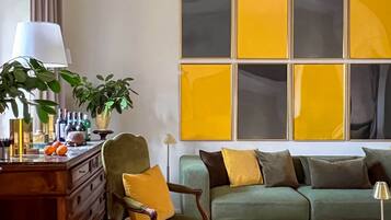 Ein Wohnzimmer mit einem grünen Sofa, einem Holzstuhl, einem Holztisch mit Lampe und einem großen abstrakten Gemälde an der Wand.