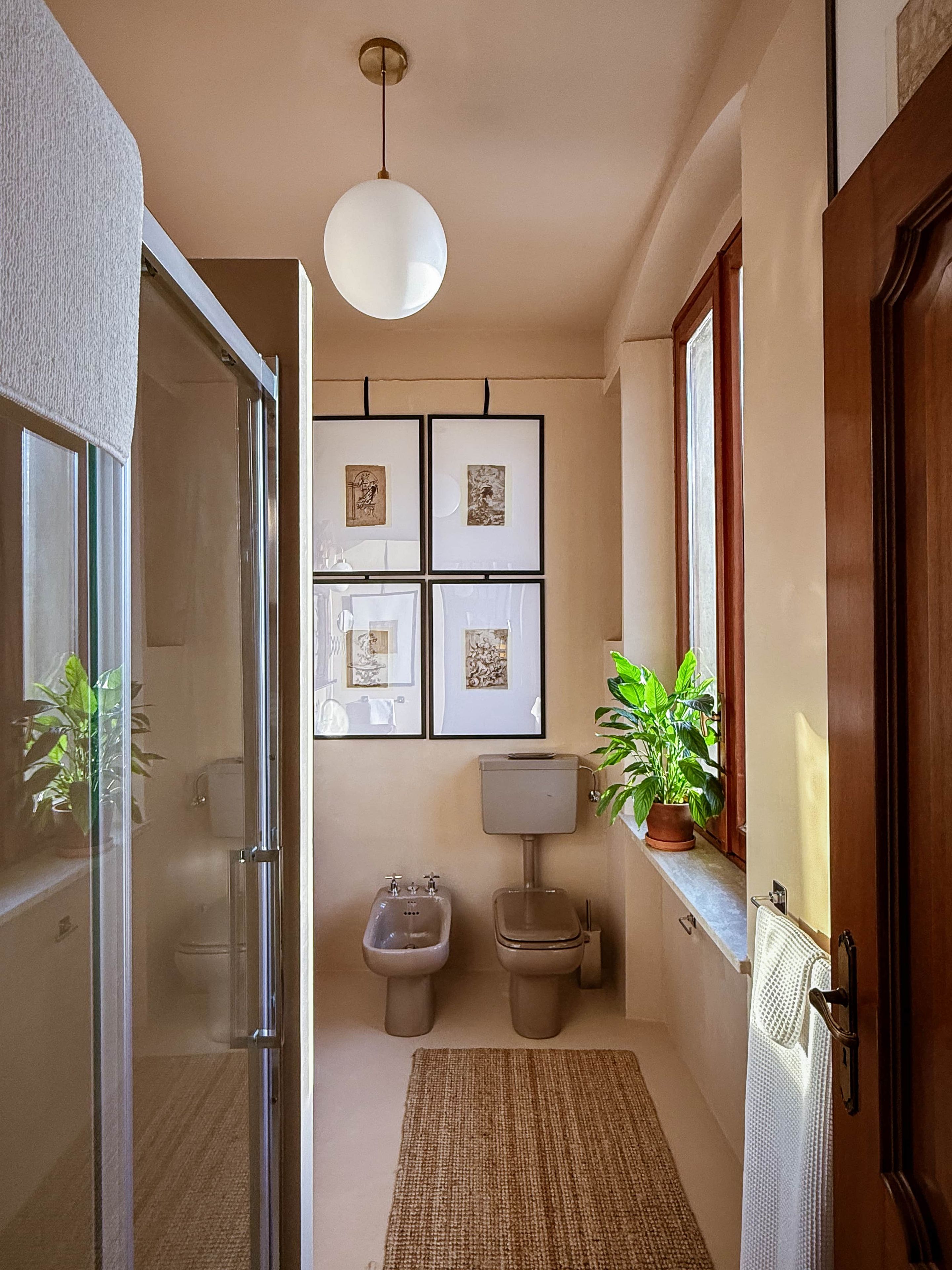 Un bagno stretto con un WC, un bidet e un lavandino, una lampada a sospensione e un'opera d'arte incorniciata al muro.