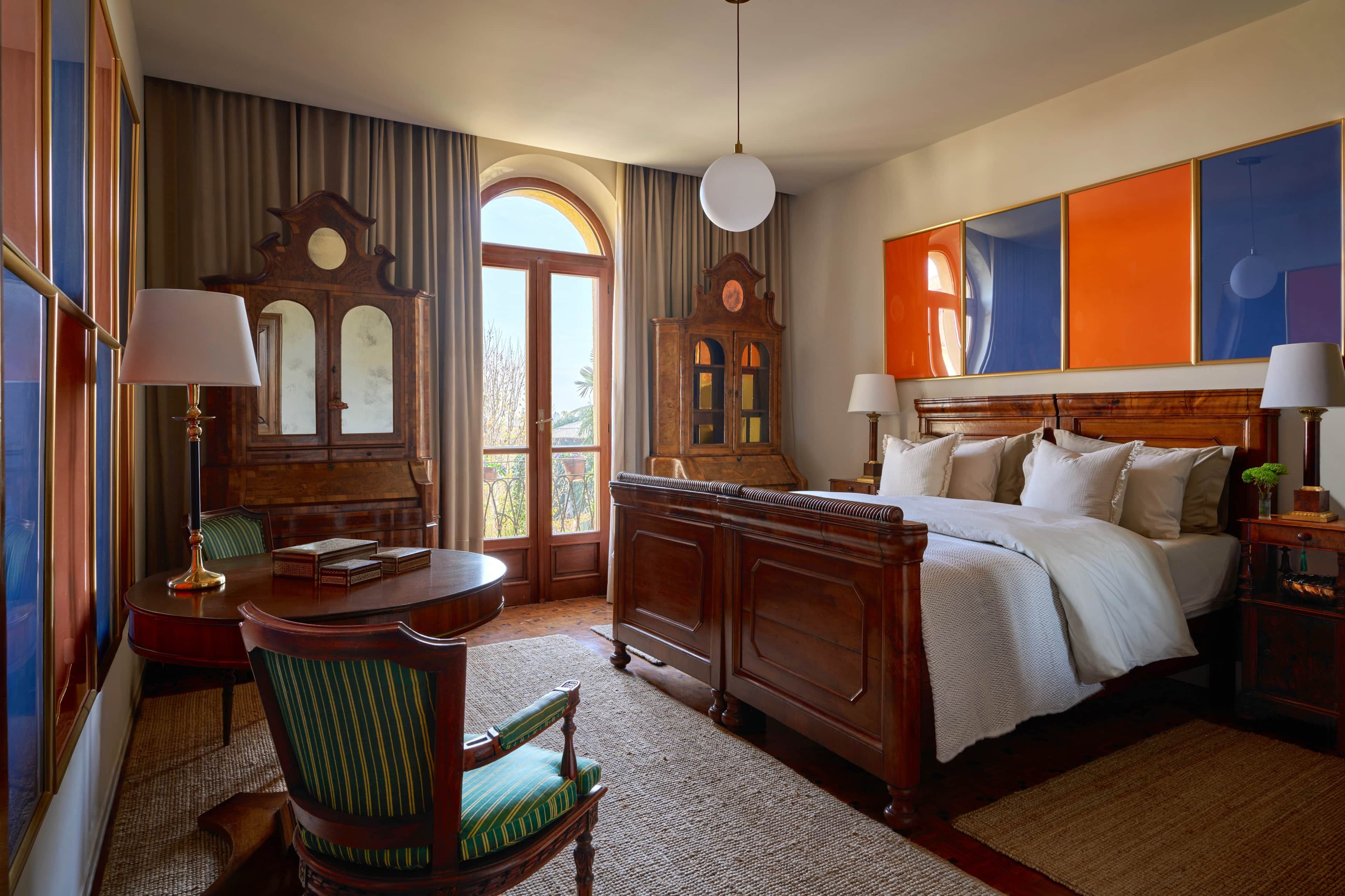 Una camera d'albergo con un letto grande, una scrivania in legno, una sedia, una lampada da scrivania, una sveglia e vista sull'esterno.