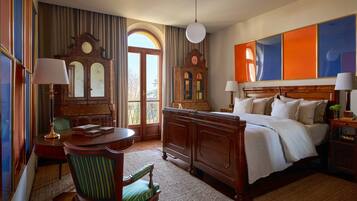 Una camera d'albergo con un letto grande, una scrivania in legno, una sedia, una lampada da scrivania, una sveglia e vista sull'esterno.