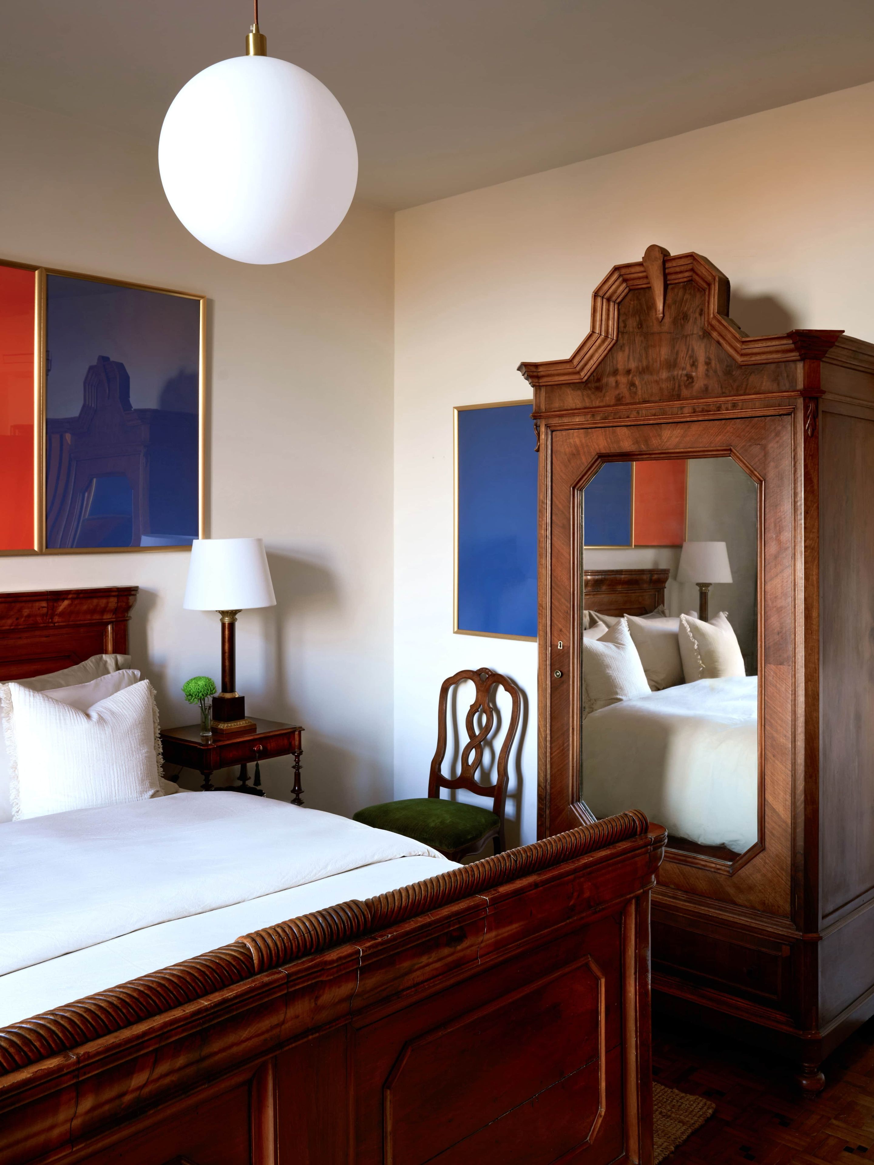 Una camera d'albergo con un letto grande, un armadio in legno, un comodino con una lampada e uno specchio.