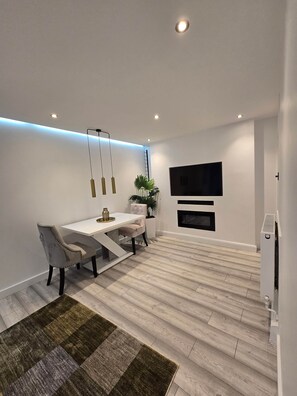 A modern living room with a dining area, a flat-screen TV mounted on the wall, and a fireplace. - Pedro's Place Battersea (London)