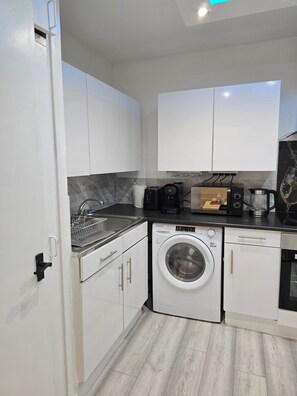 A modern kitchen with white cabinets, a built-in washing machine, a coffee maker, and a toaster. - Pedro's Place Battersea (London)