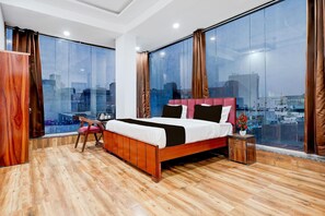 Une chambre moderne avec un grand lit, un plancher en bois et une vue sur la ville grâce à de grandes fenêtres du sol au plafond.